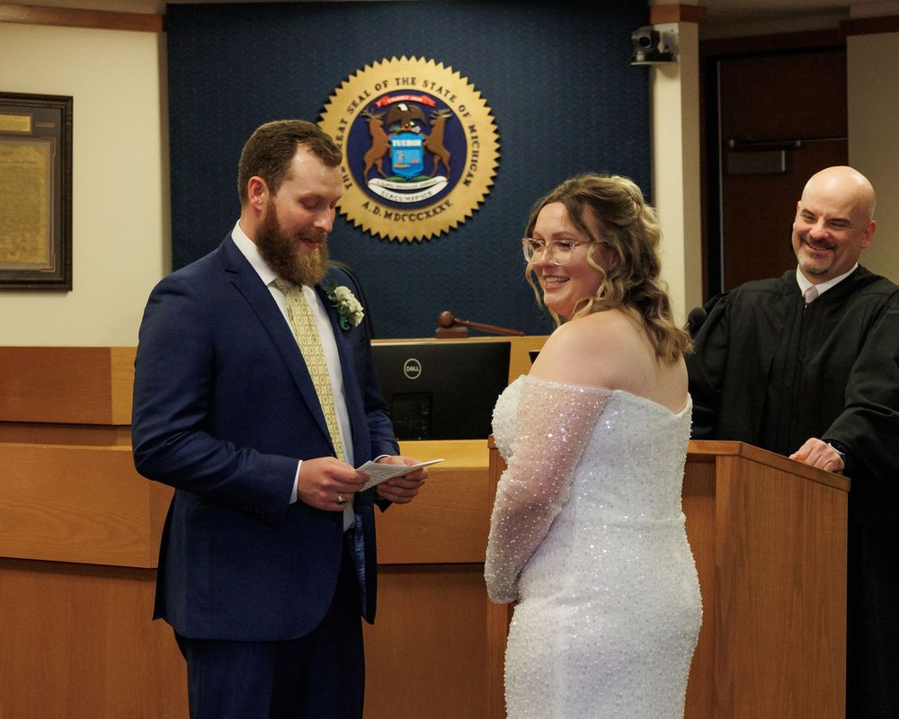 A couple exchanges rings during an intimate civil ceremony in front of an officiant in a courthouse.