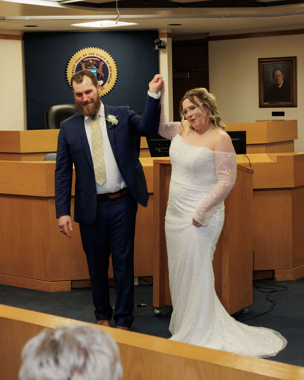 A couple celebrates their wedding ceremony in a room with a navy blue wall featuring a gold circular emblem.