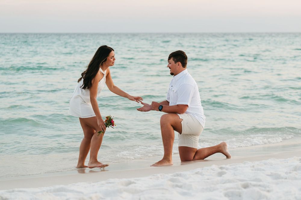 A marriage proposal unfolds on a pristine beach with turquoise ocean waters in the background.