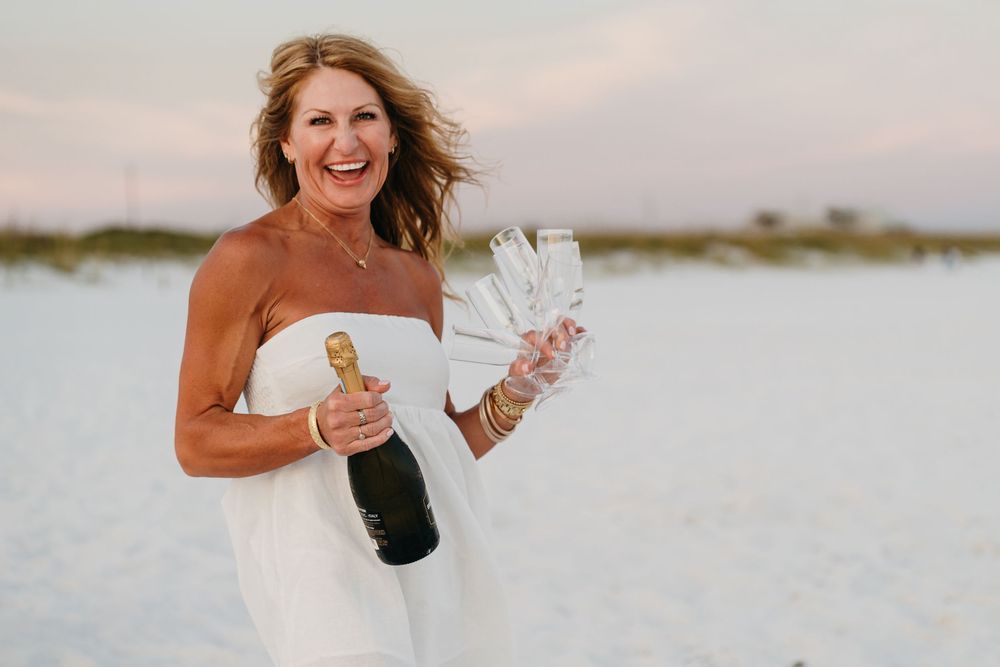People celebrating and popping champagne bottles on a beach at sunset.
