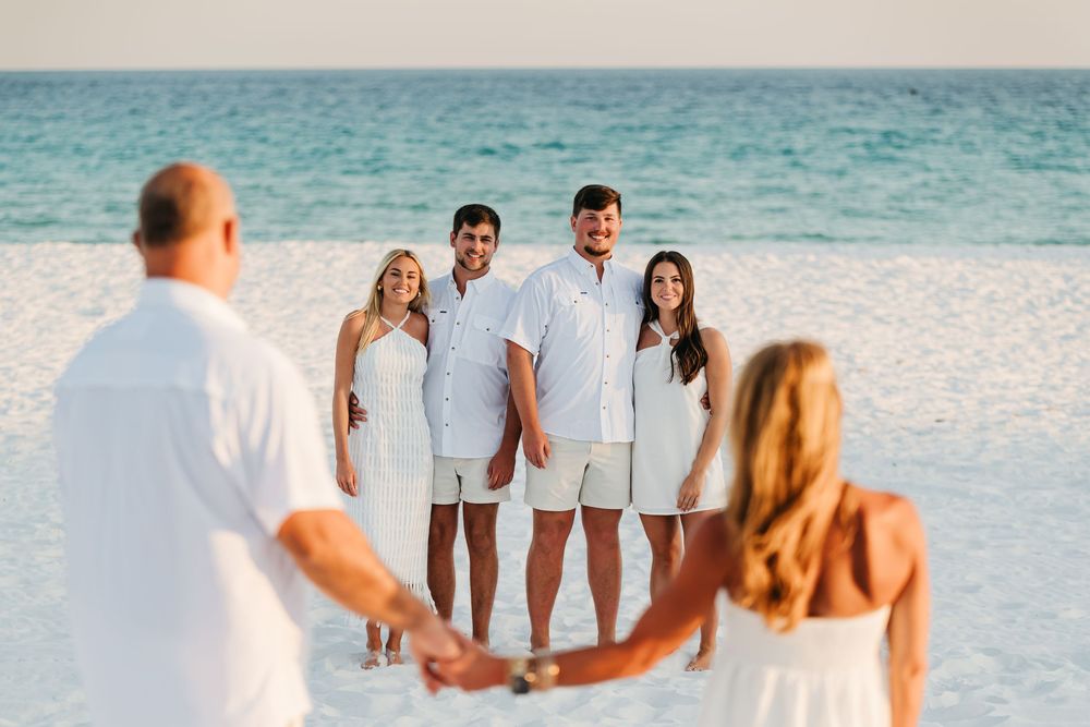 A group in white outfits walking along a pristine beach with turquoise waters in the background.