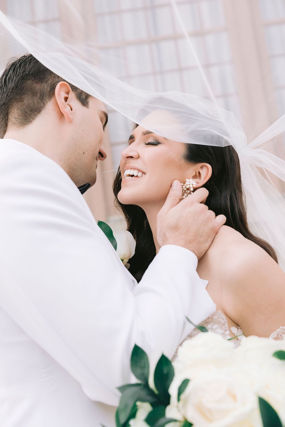 Romantic wedding moment captured under flowing white veil with soft natural lighting.