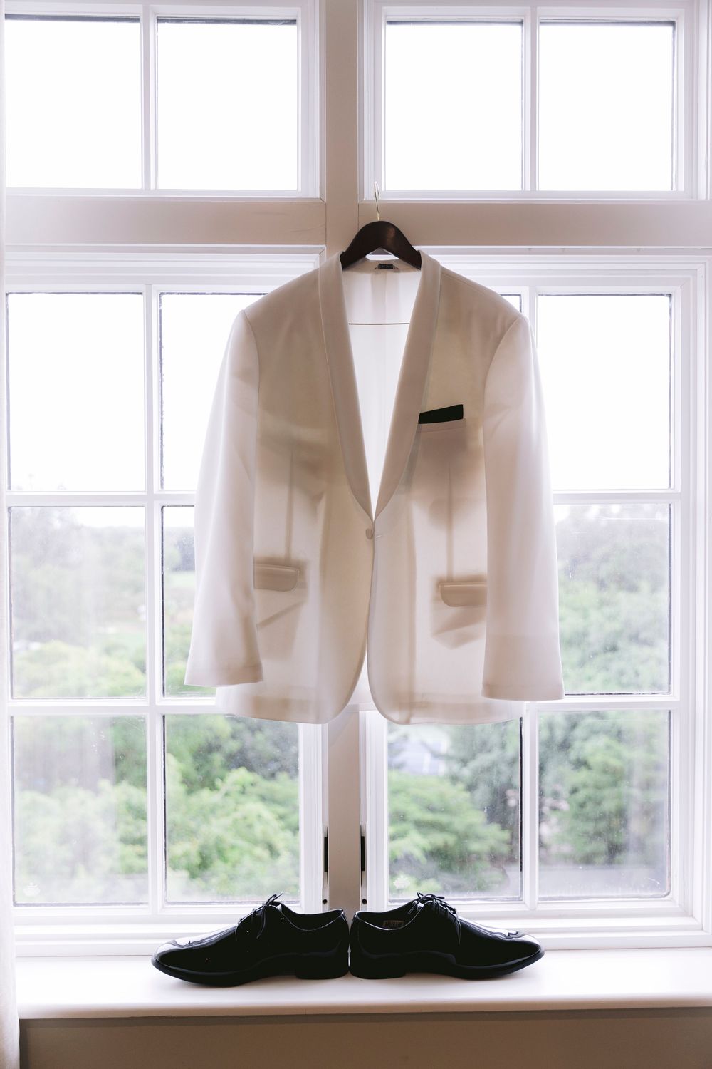 White wedding attire and formal shoes displayed near bright windows in a dressing room.