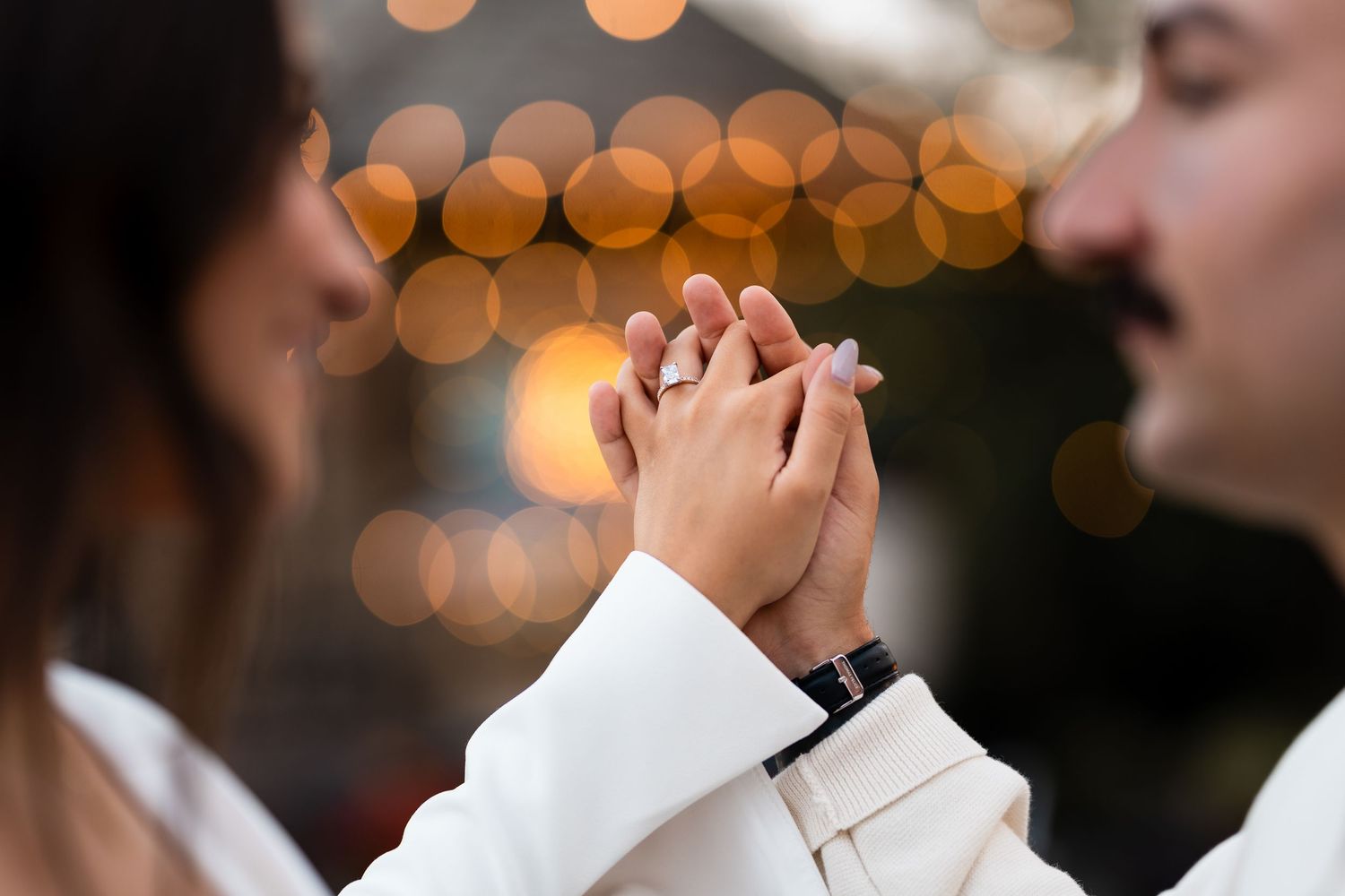 Close-up of hands during first dance with soft bokeh lights in background.