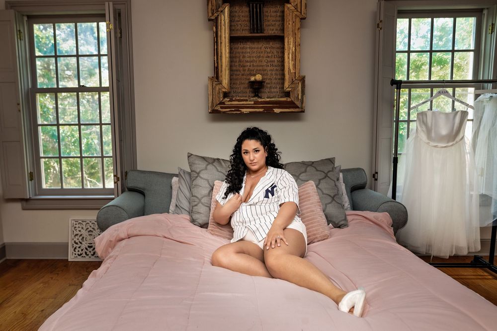 Boudoir photography session featuring soft pink bedding in an elegant room with large windows.