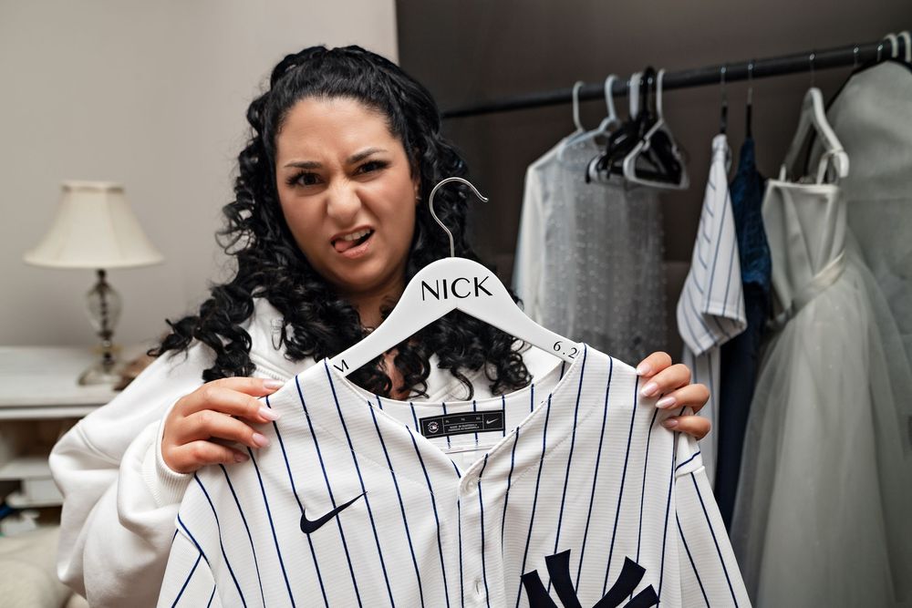 A person holds up a pinstriped Nike New York Yankees baseball jersey in a closet or dressing room.