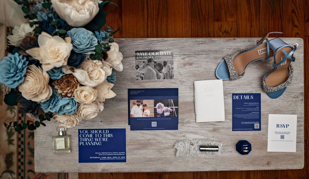 Wedding details display with blue and white flowers, paper goods, and decorative elements on a wooden surface.