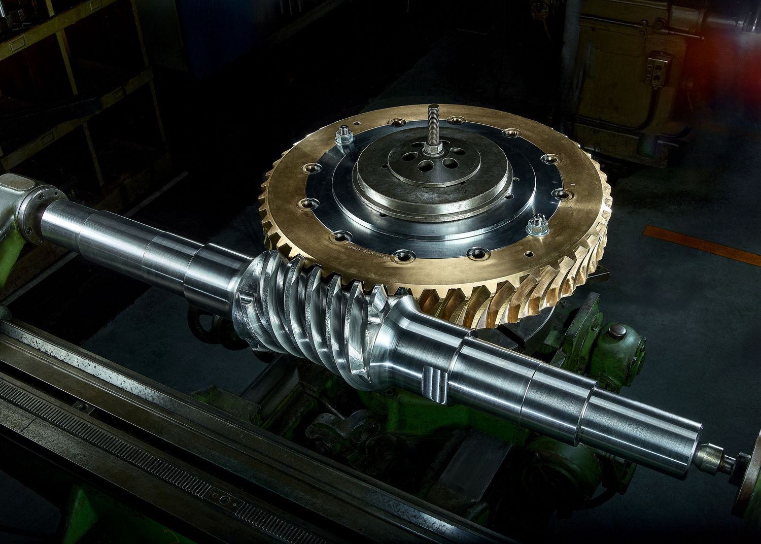 Closeup view of a metal gear assembly with shafts and mechanical components in a dark industrial setting.