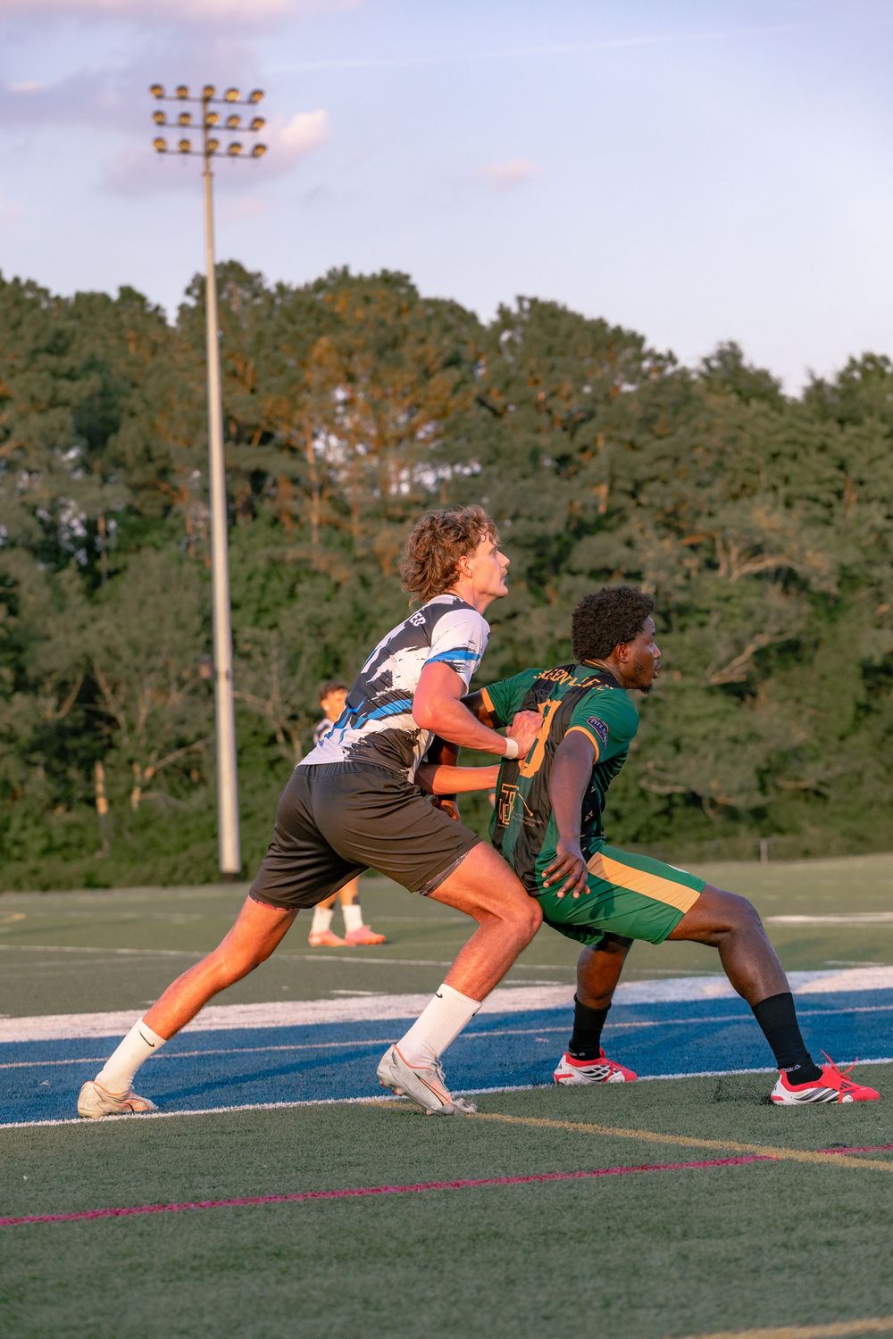 Two youth flag football players compete on a blue turf field under stadium lights at dusk.