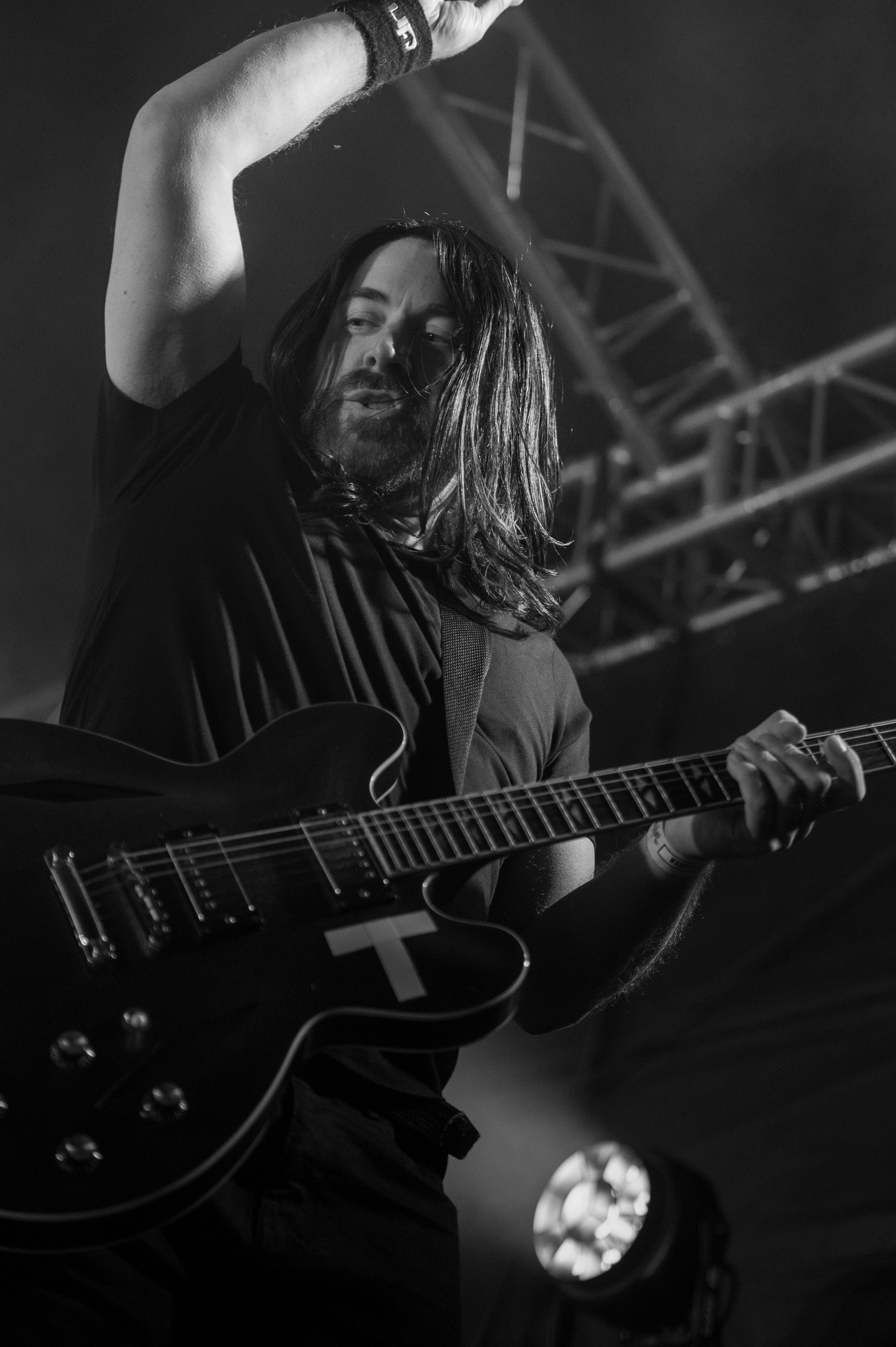 Black and white photos of a guitarist performing on stage with a dark acoustic guitar under dramatic lighting.