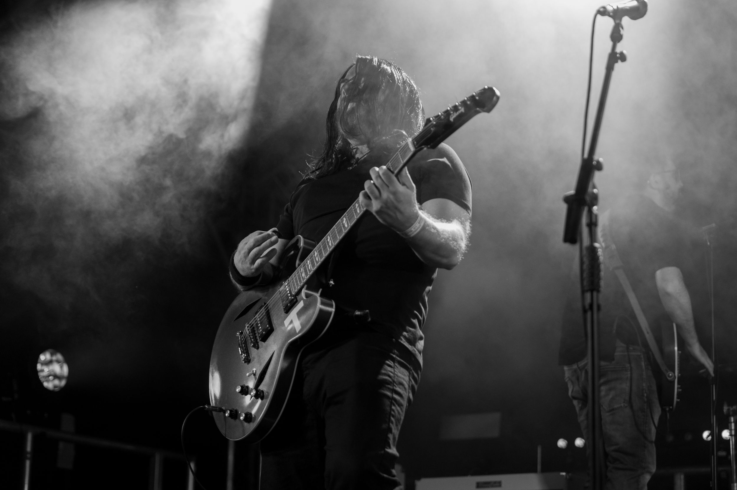 A musician performs on stage with an electric guitar amid atmospheric smoke during a concert performance.