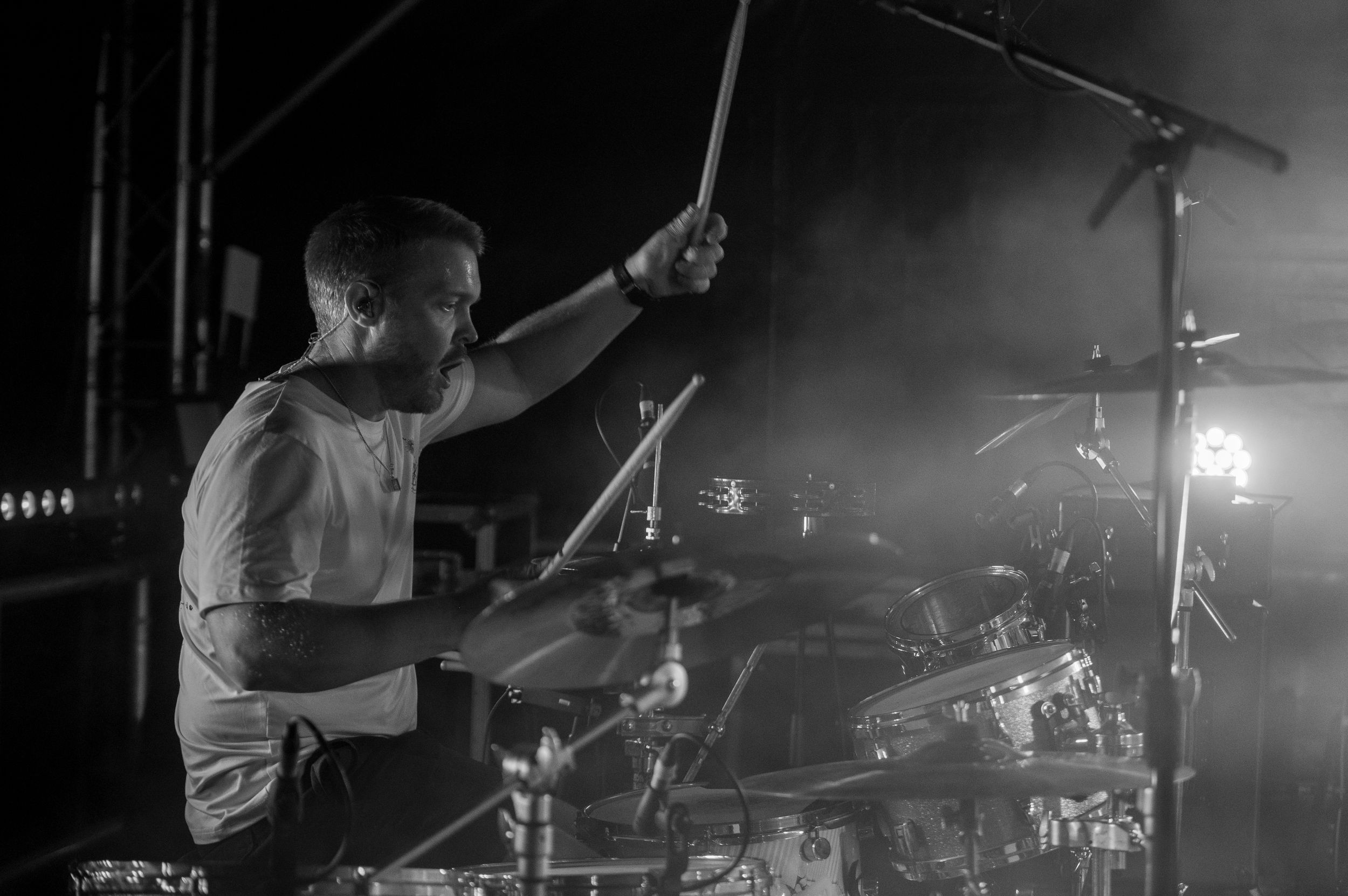 Drummer performs energetically on stage with dramatic lighting and smoke effects during a live concert performance.