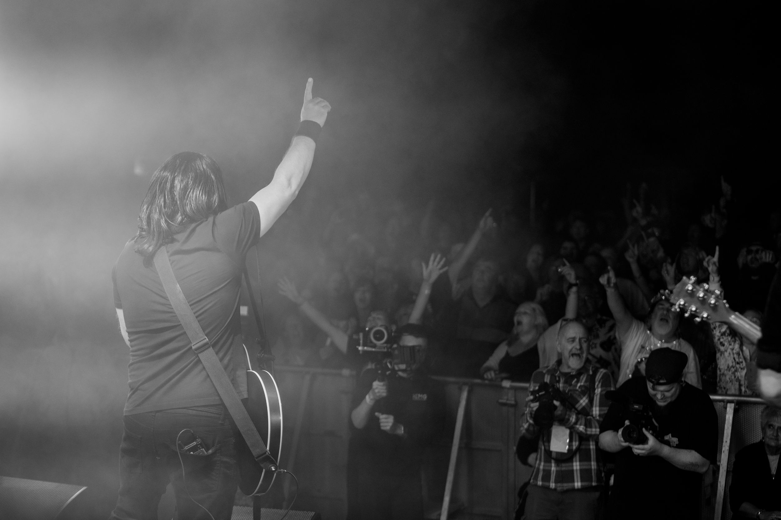 Black and white concert scene with performers on stage illuminated by dramatic spotlights during an energetic performance.