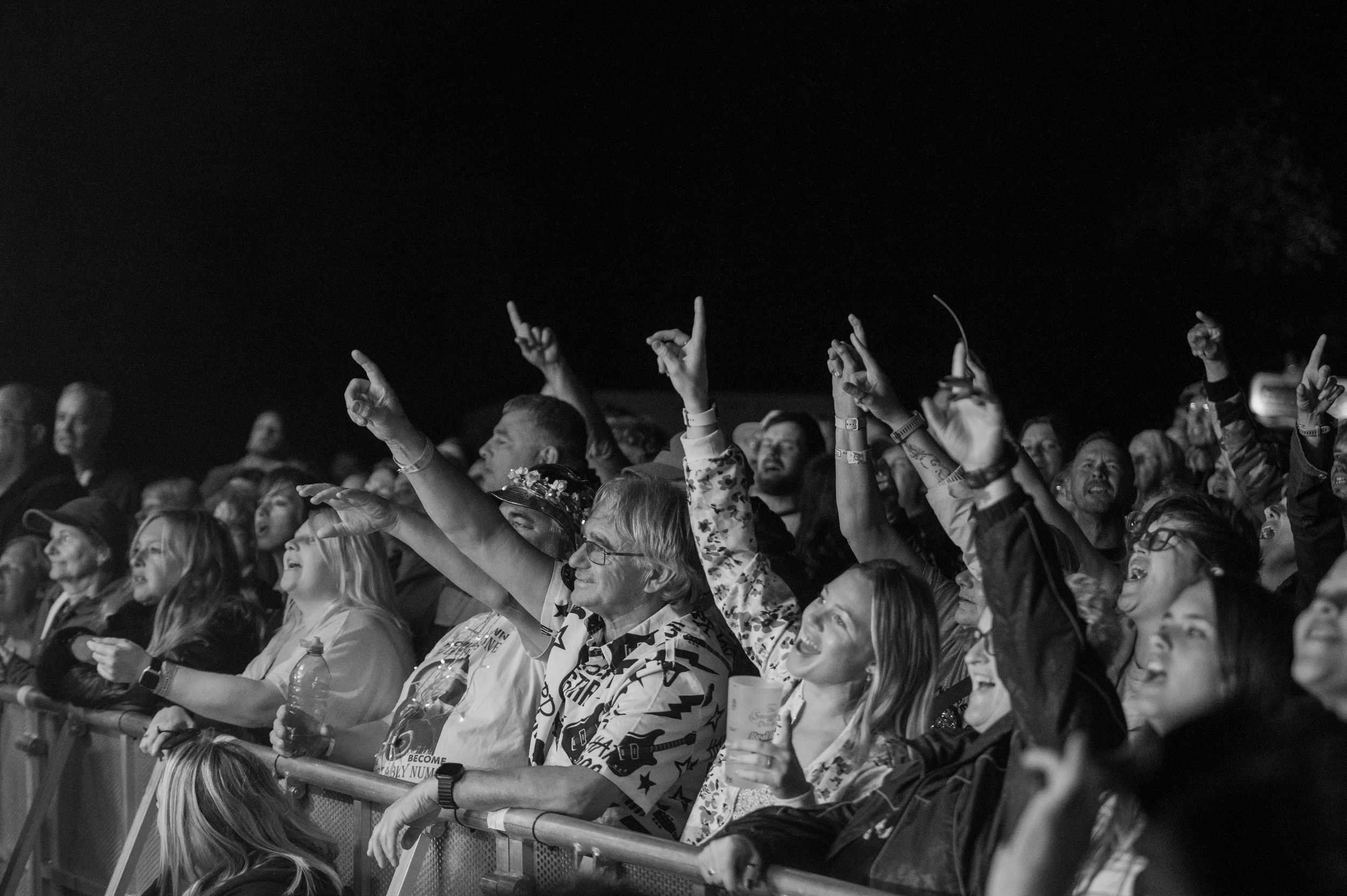 Concert crowd at a rock show throwing up devil horns hand gestures while enjoying live music performance.