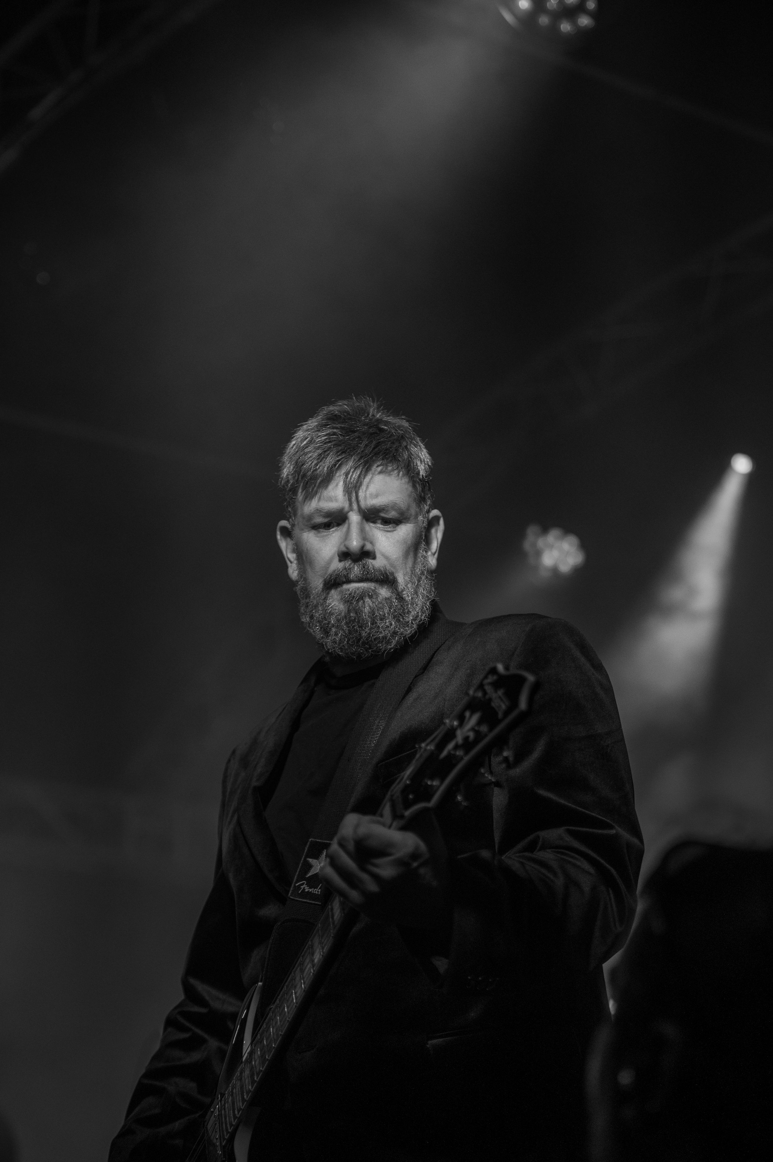 Black and white concert photo of a performer in dark clothing playing on stage with dramatic lighting.