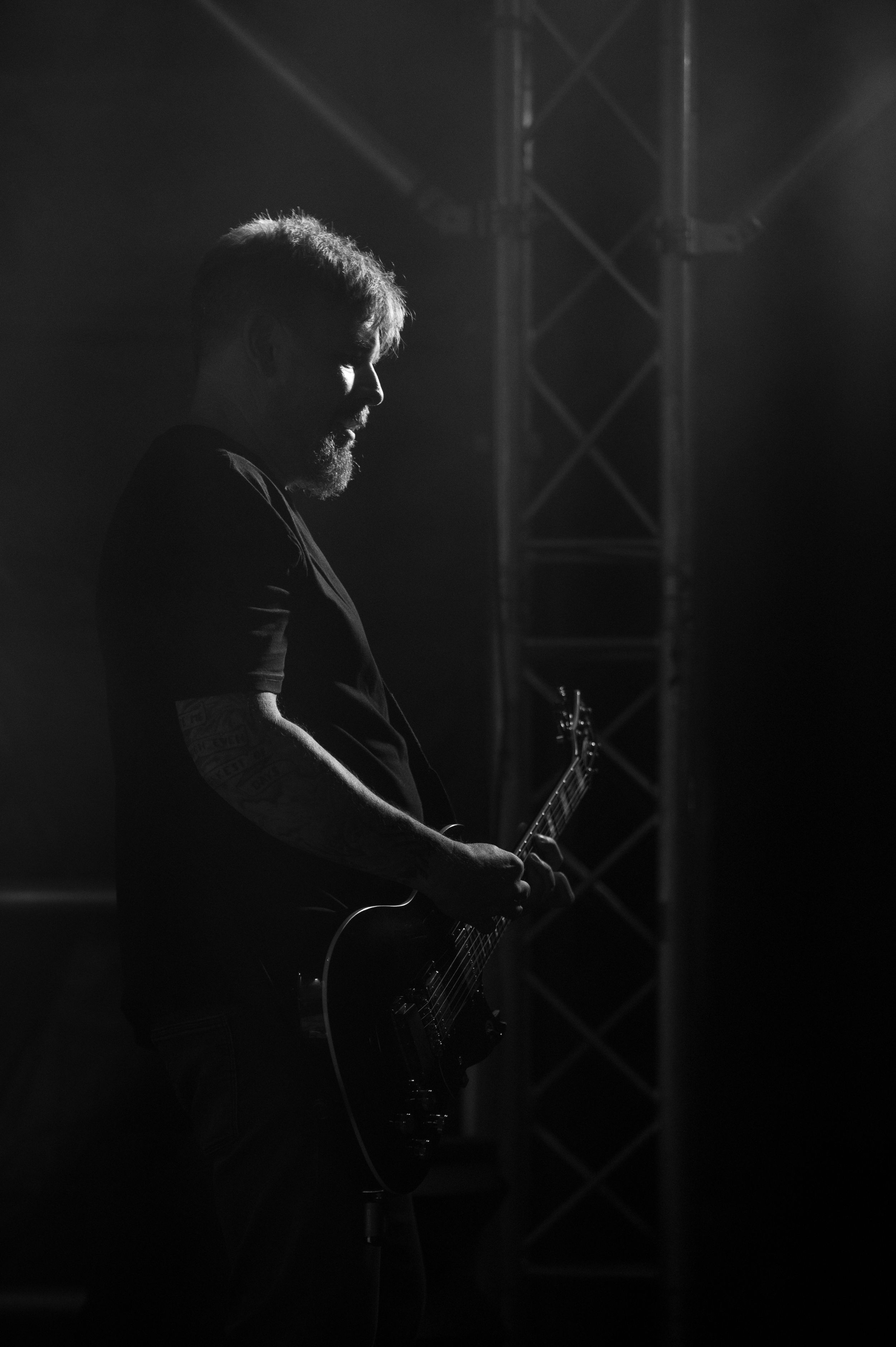 A dramatic black and white silhouette of a guitarist performing on stage with moody lighting and fog effects.