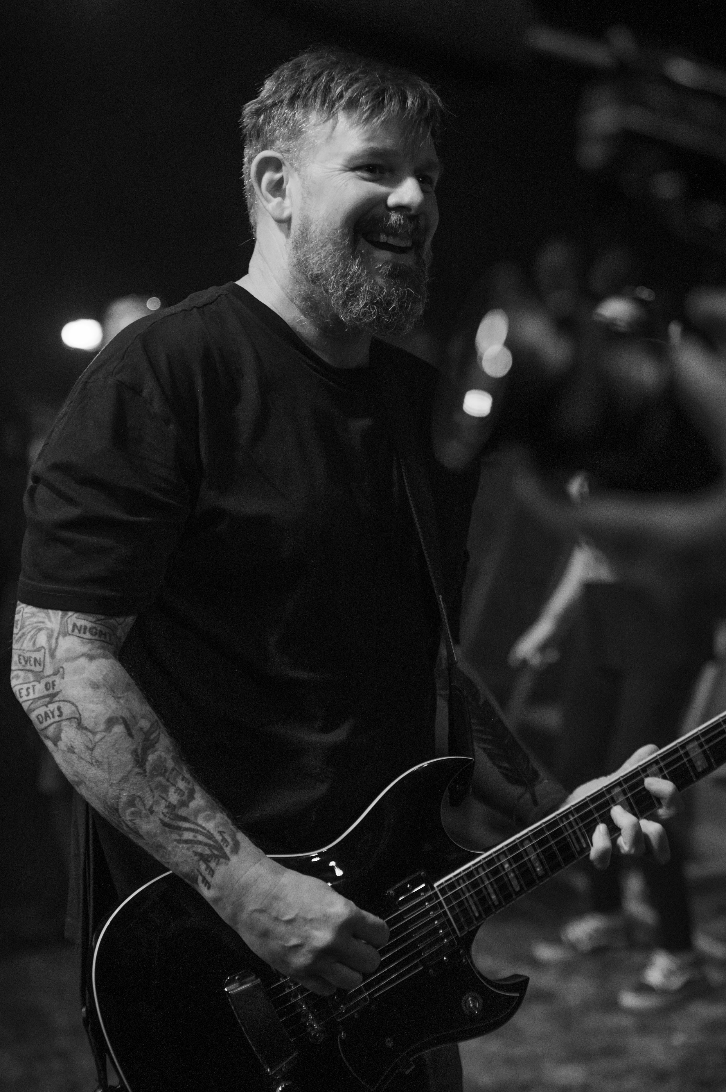 Black and white photos of a tattooed musician playing bass guitar during a live performance.