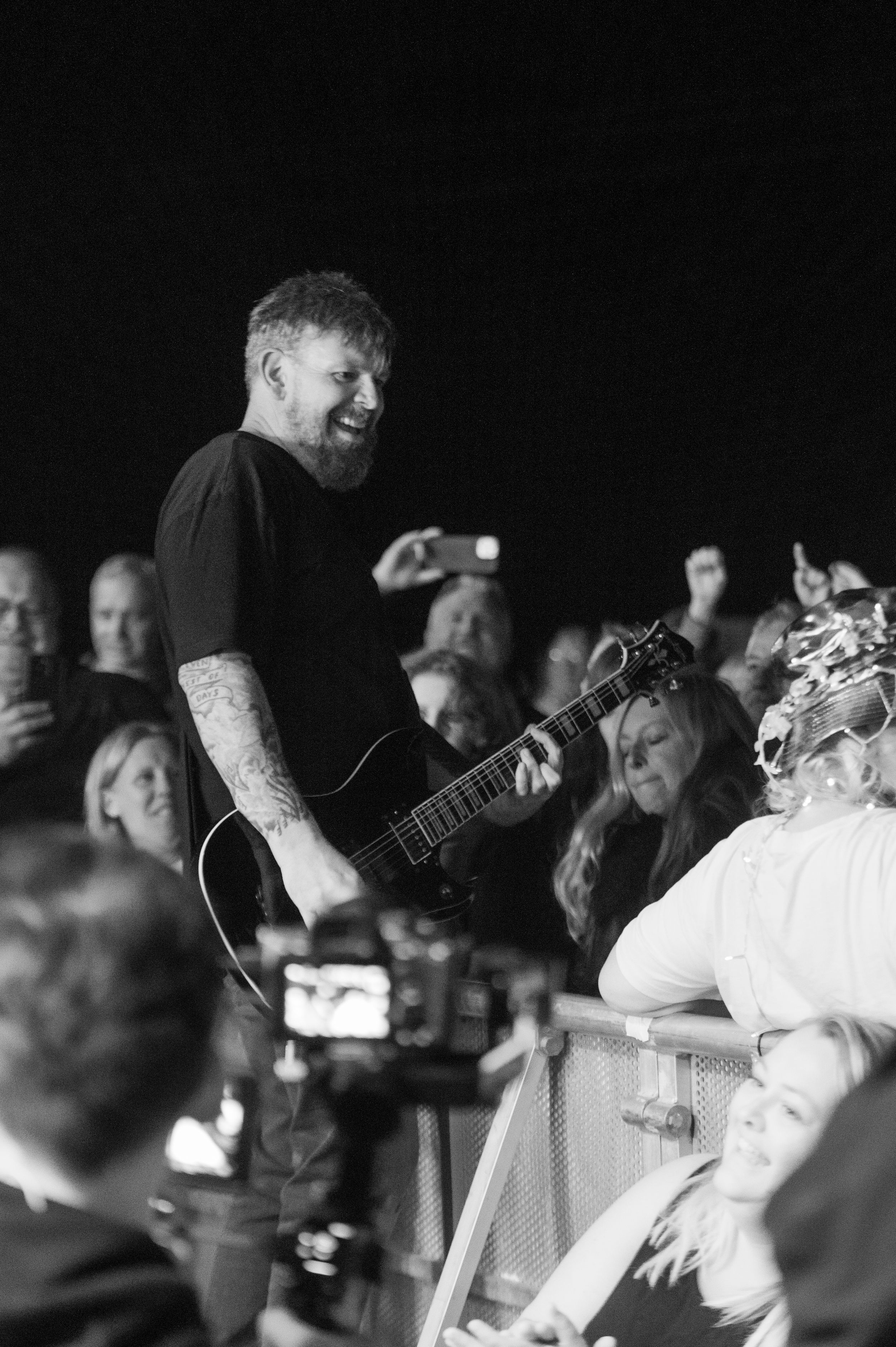 Concert crowd and performers captured in monochrome with dramatic stage lighting and silhouettes.