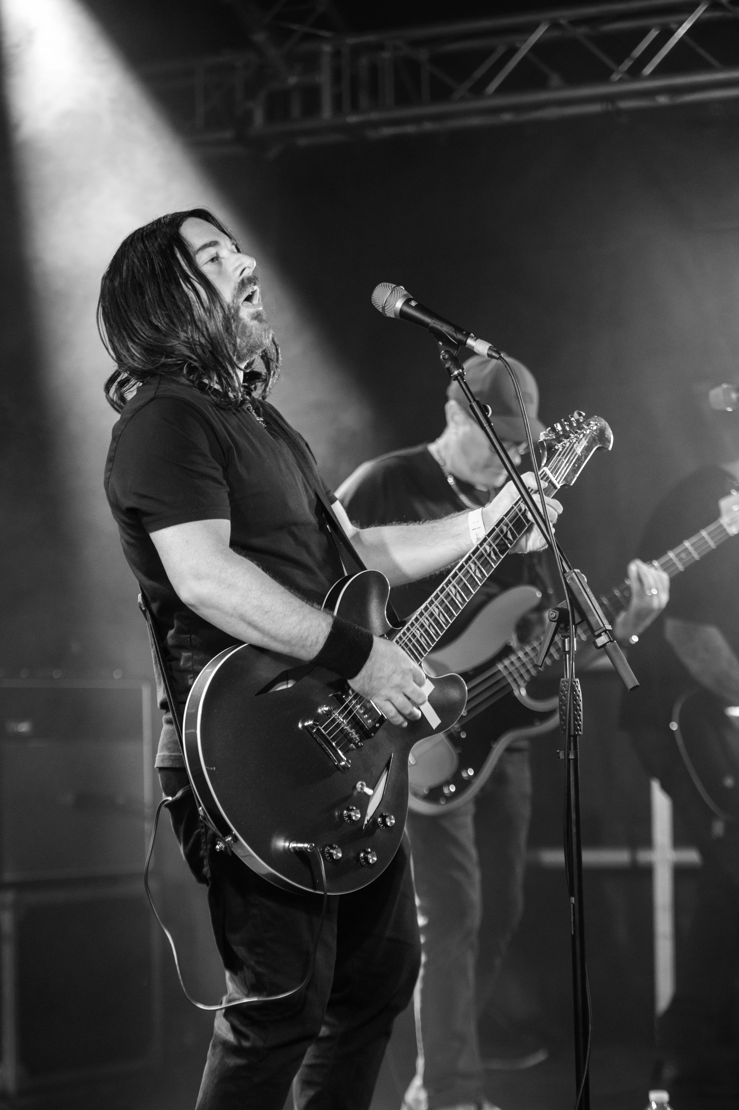 Black and white photo of a musician performing on stage with a guitar under dramatic lighting.