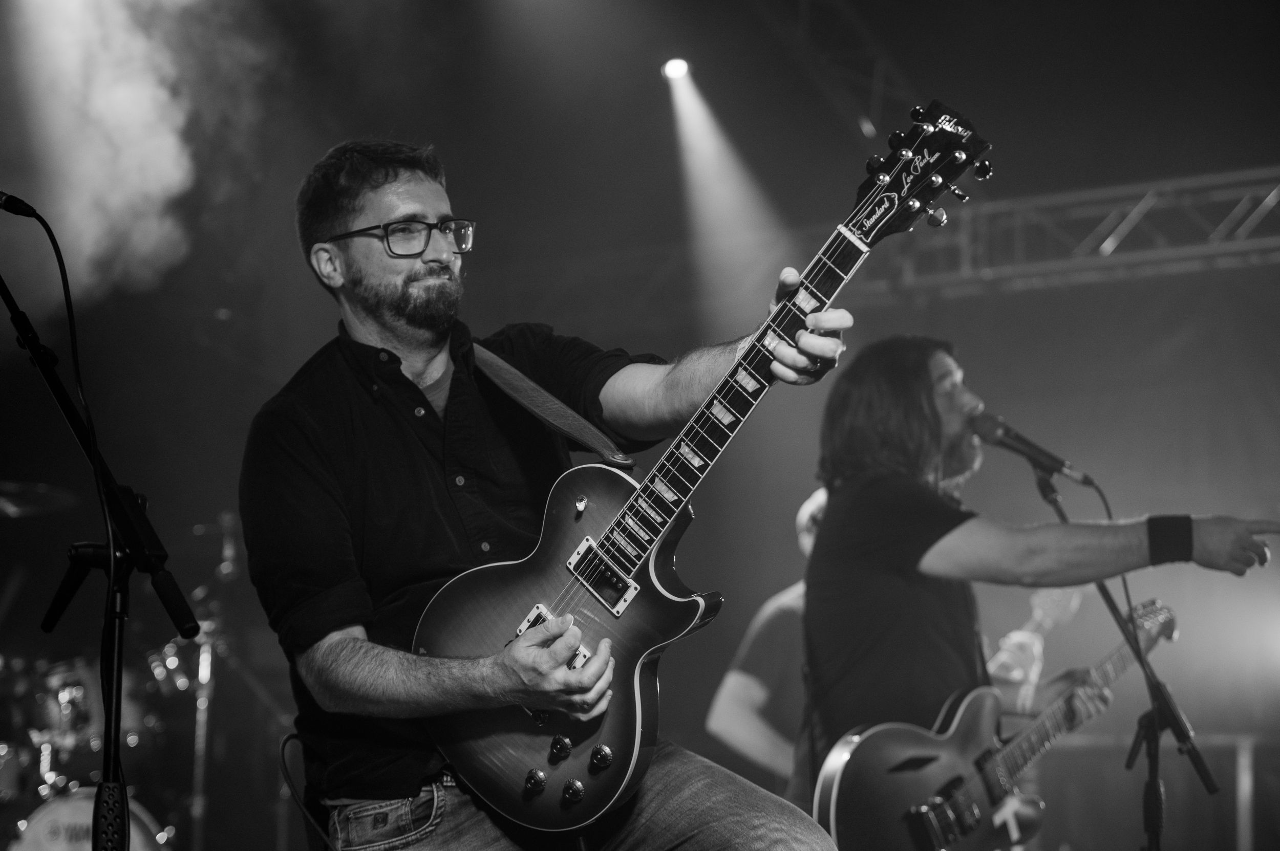 Black and white photo of a guitarist performing on stage with an electric guitar and dramatic lighting.