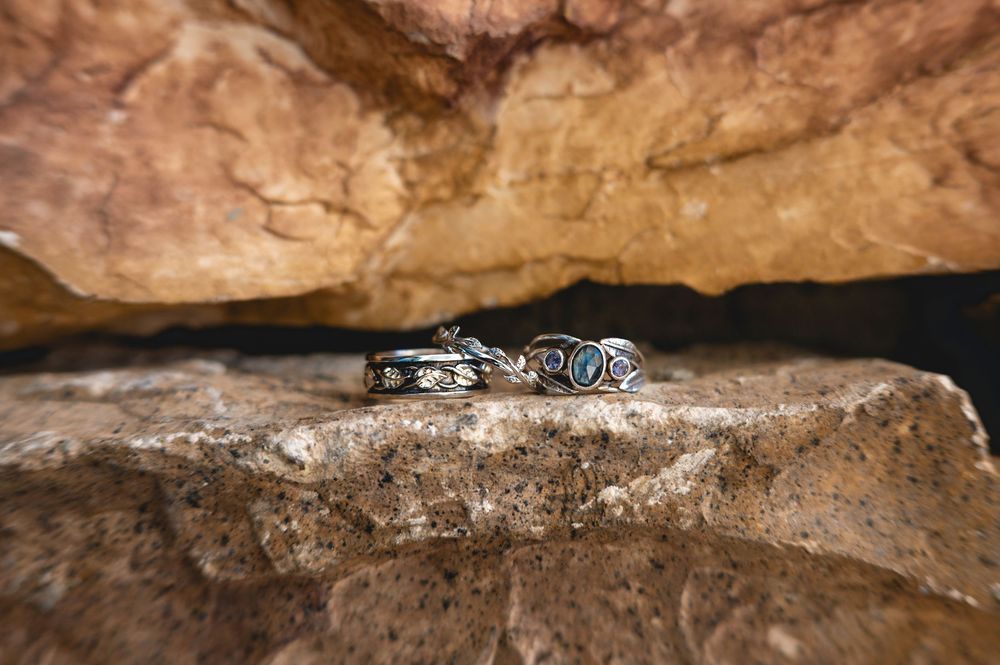 Diamond engagement ring and wedding band displayed on textured brown stone in a cave-like setting.