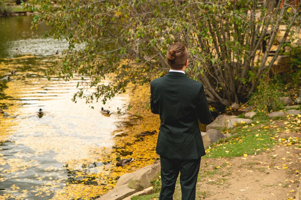 People walking along a tranquil pond path surrounded by fall foliage and golden evening light.