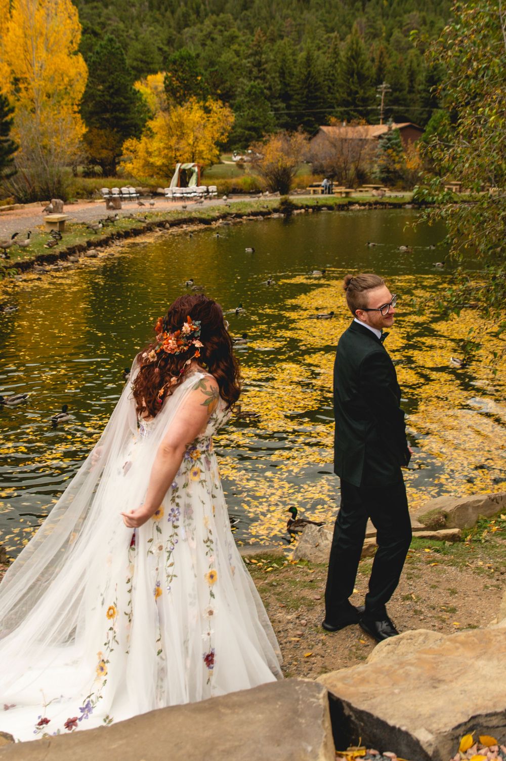 A couple shares a romantic moment by a lake surrounded by golden autumn foliage reflecting on the water's surface.