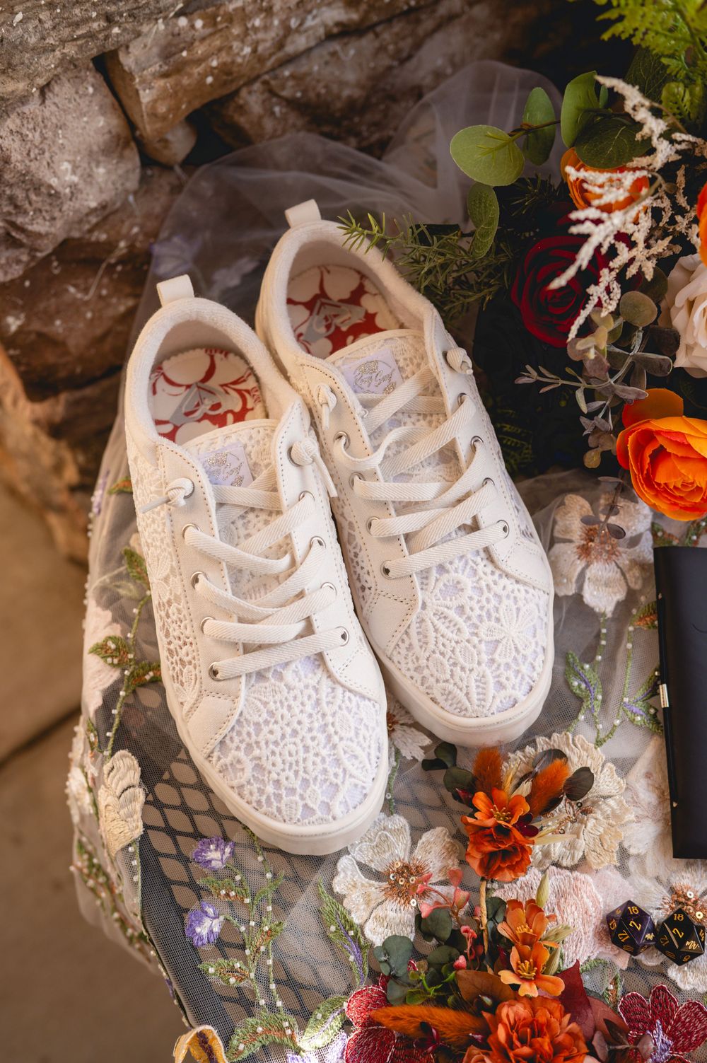 Small white baby shoes decorated with lace and floral patterns displayed among autumn flowers and decorative elements.