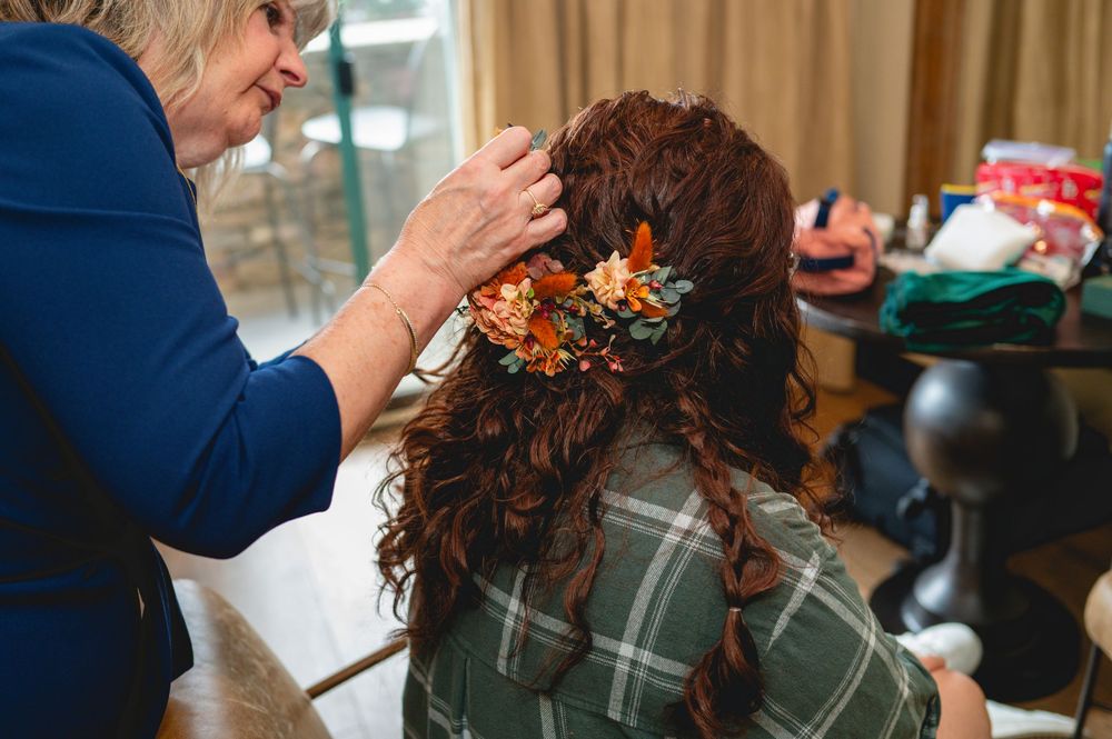 A person's hands carefully style curly brown hair with orange floral accessories in a salon setting.