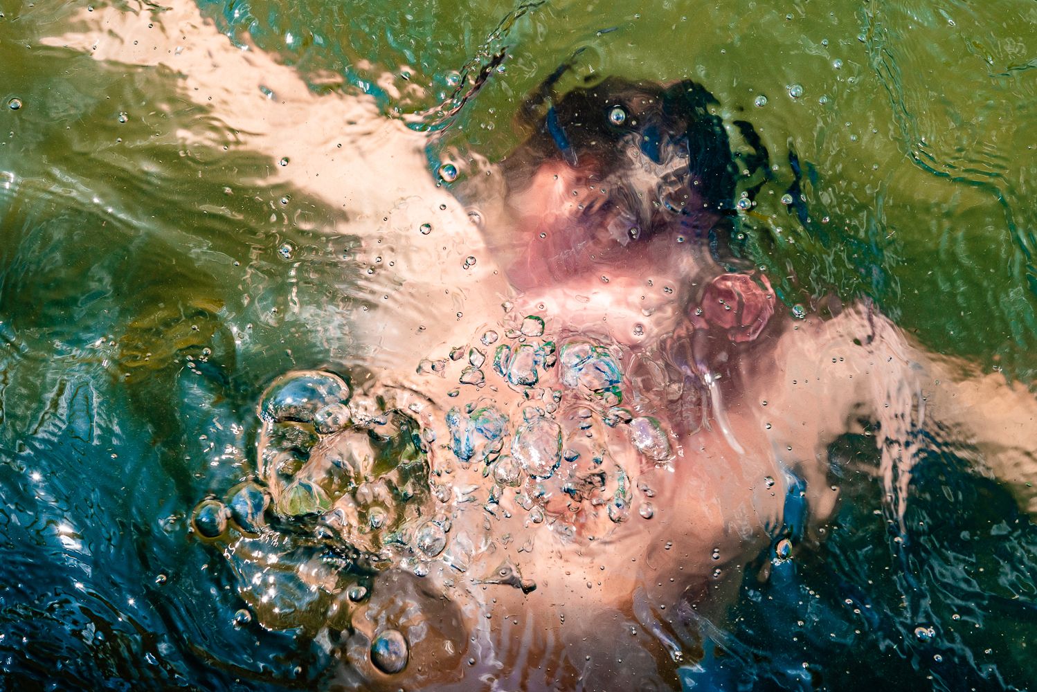 Abstract aerial view of colorful water with pink and green hues creating a swirling pattern in natural lighting.