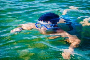 Someone swimming underwater in clear turquoise water wearing blue goggles and dark hair.