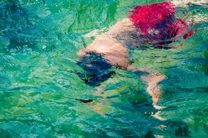 Abstract underwater view of a swimmer in turquoise water with splashes of red and pink colors visible from above.