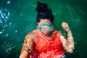 Swimmer in bright red tank top floating in turquoise water wearing a snorkel mask.