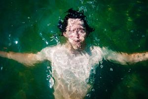 Person swimming underwater in emerald green water with arms spread wide creating bubbles around them.