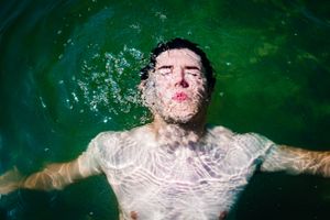 Underwater view of someone floating in green-tinted pool water with rippling surface effects around them.