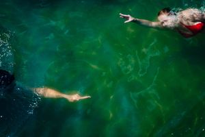 Aerial view of two swimmers gliding through emerald green waters with rippling reflections.