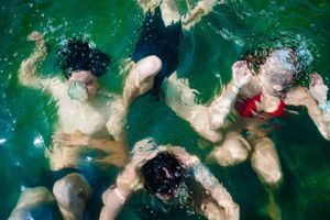 People swimming underwater in green tinted water with bubbles and dynamic movement captured in an artistic shot.