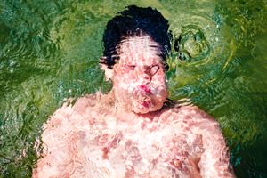 A person swimming underwater with air bubbles rising around them in green-tinted water.