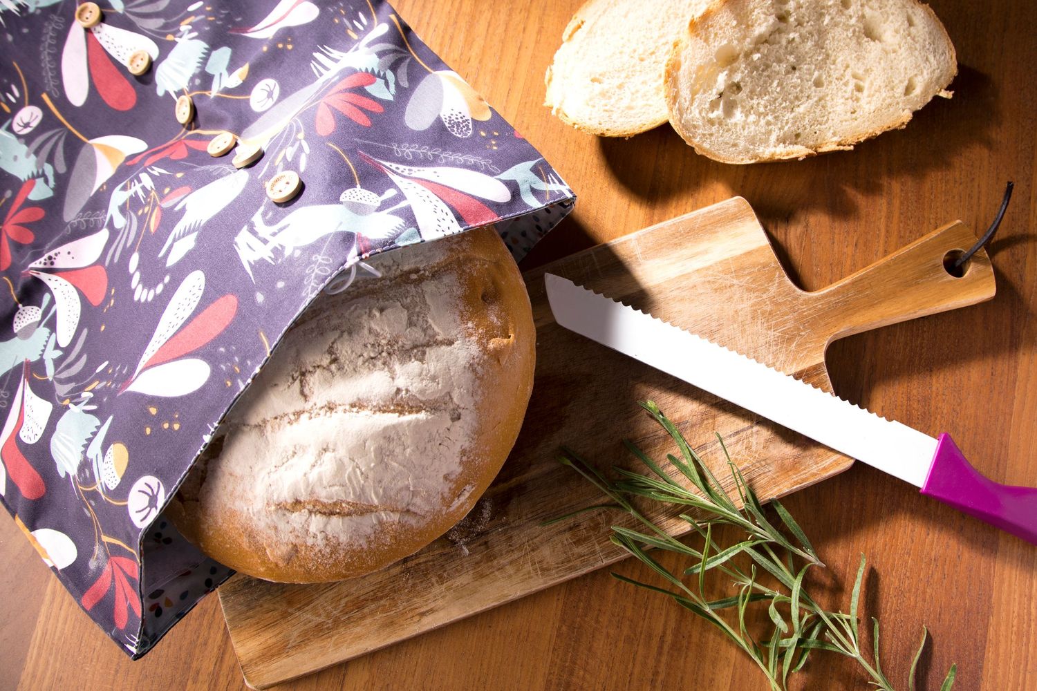 Pain artisanal frais sur planche à découper en bois avec sac à pain en tissu à motifs floraux et herbes.