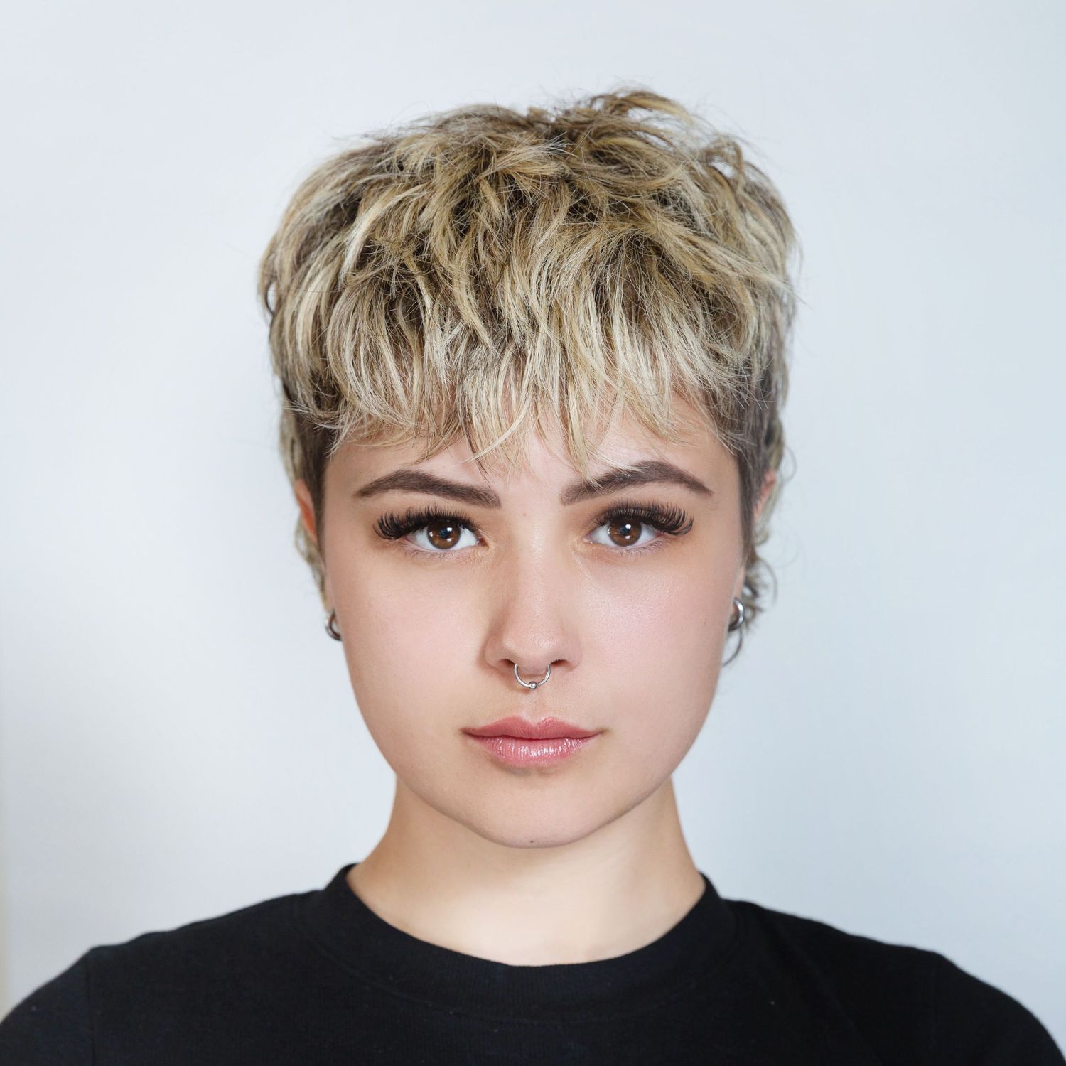 Studio portrait of person with short blonde pixie cut wearing black top against white background.