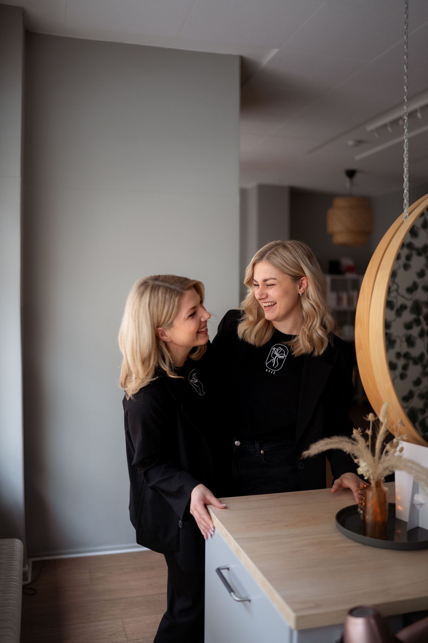 Two people wearing black outfits share a joyful moment together in a modern interior setting with natural lighting.