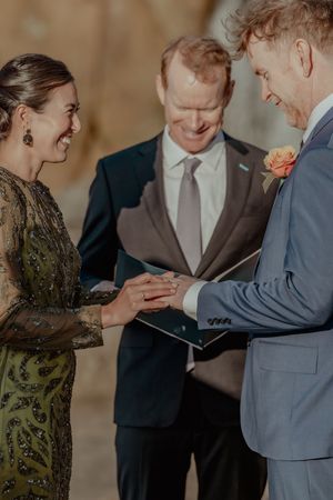 A couple exchanges rings during an intimate wedding ceremony with an officiant in formal attire.