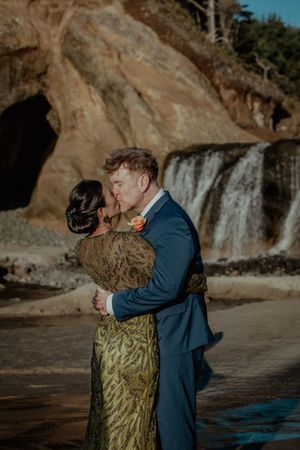 A romantic moment captured at a scenic waterfall beach location with dramatic cliffs and natural scenery.