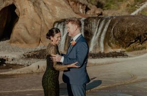 Romantic couple shares an intimate moment against rocky coastal cliffs at sunset.