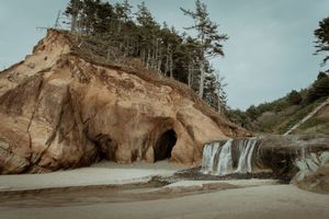 Scenic coastal waterfall cascades down rocky cliffs at Hug Point State Park in Oregon during golden hour.