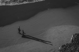 Black and white photograph of people walking on sandy beach dunes casting long shadows.