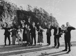 A wedding party stands in line on a path against a scenic mountain backdrop in black and white.