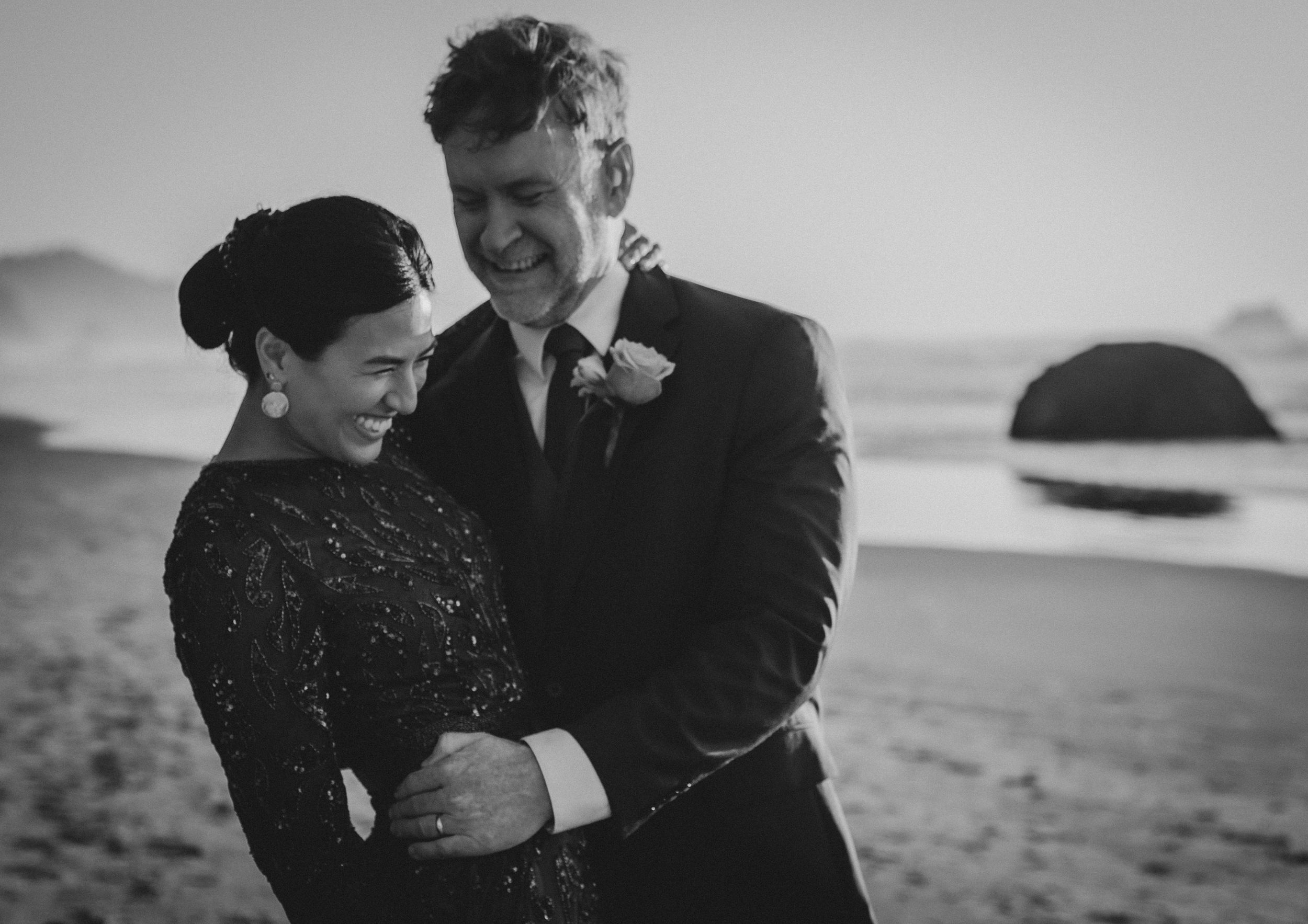 Black and white romantic portraits on a moody coastal beach with rock formations in the background.