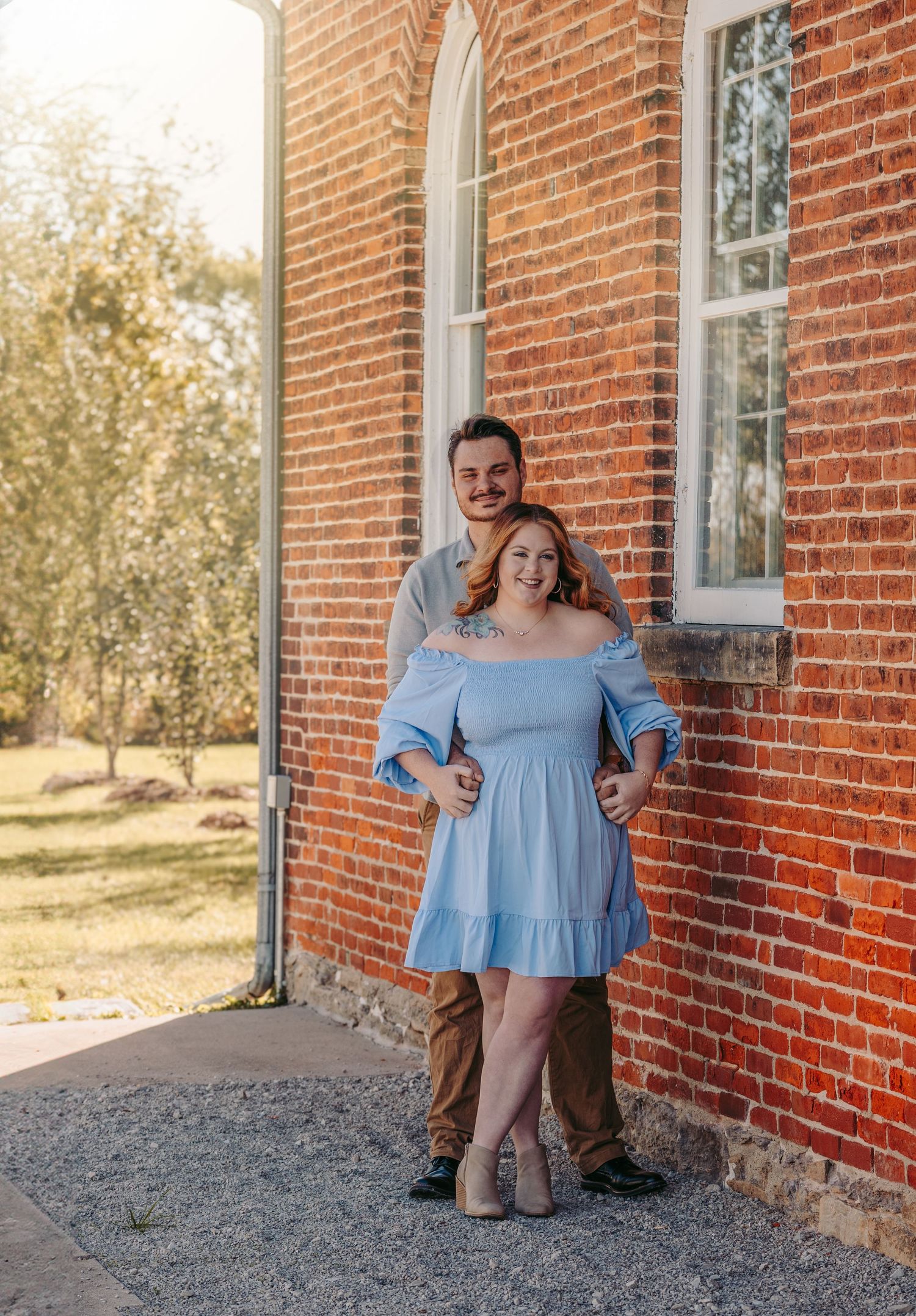 A couple poses for an engagement photo against a rustic brick church exterior.