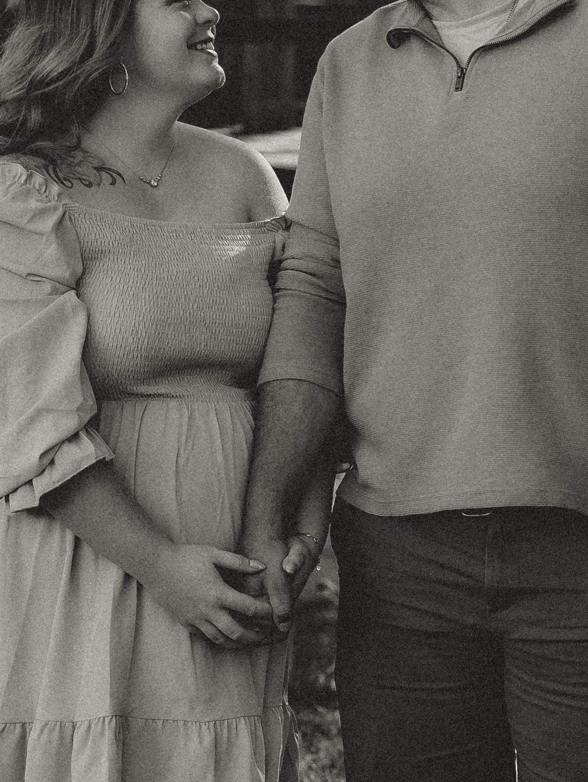 A black and white romantic portrait of a couple in casual clothing holding hands.